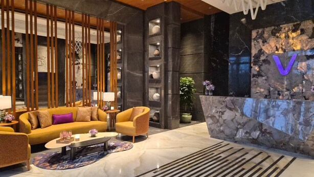 A modern lobby with a reception desk, a sofa, armchairs, a coffee table, and a patterned rug. - Vivanta Gurugram, Sector 95A (Gurugram)