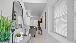 A hallway with a light-colored floor, a grey sofa, a white console table with decorative items, and a large mirror. - Cozy, Comfy, Warm Relaxing Home (Conroe)