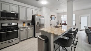 A modern kitchen with stainless steel appliances, a granite countertop, and a bar area with stools. - Cozy, Comfy, Warm Relaxing Home (Conroe)