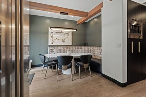A modern kitchen with a dining area, featuring a wooden ceiling, a wall-mounted light fixture, and a patterned backsplash.
