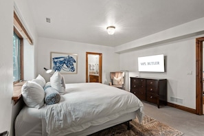 A bedroom with a large bed, a dresser, a mirror, and a wall-mounted TV.