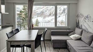 Ett modernt vardagsrum med ett matbord, en soffa och stora fönster med utsikt över bergen.
