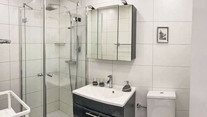 Ett modernt badrum med en duschavdelning med glasväggar, en vit tvättställskommod med ett svart skåp och en toalett.