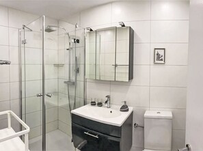 Ein modernes Badezimmer mit einer Duschkabine aus Glas, einem weißen Waschbecken mit schwarzem Unterschrank und einer Toilette.