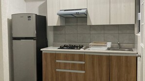 Une cuisine compacte dotée d’un réfrigérateur encastré, d’une cuisinière à gaz, de meubles en bois et d’un dosseret carrelé.