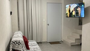 Un salon avec un canapé, un téléviseur, un escalier et une porte.