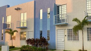 Un bâtiment moderne à la façade plate, doté de grandes fenêtres et d’un petit espace jardin agrémenté de plantes et d’un sentier.