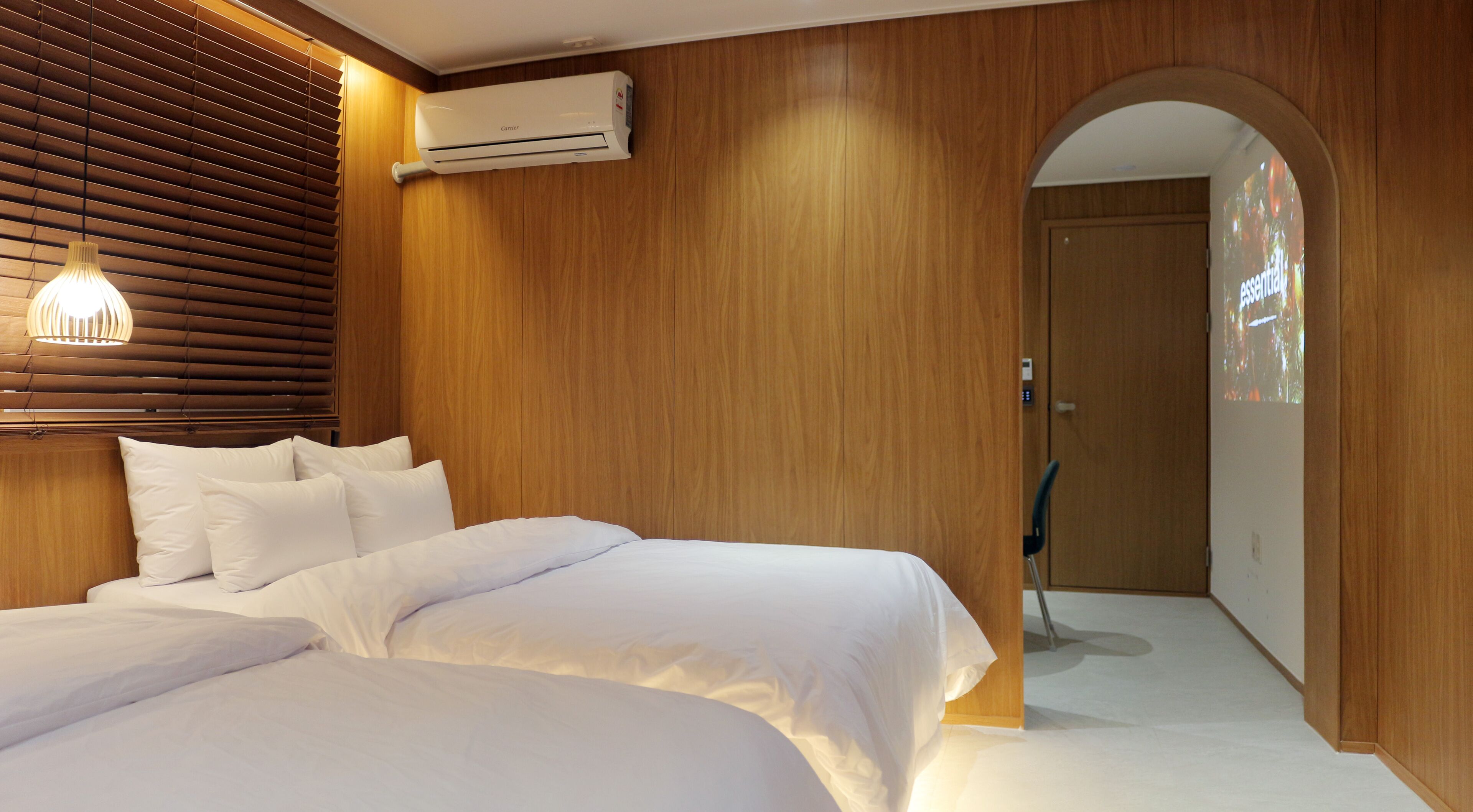 Una camera d'albergo con parete in legno, un letto con lenzuola bianche, un climatizzatore e una porta in legno.