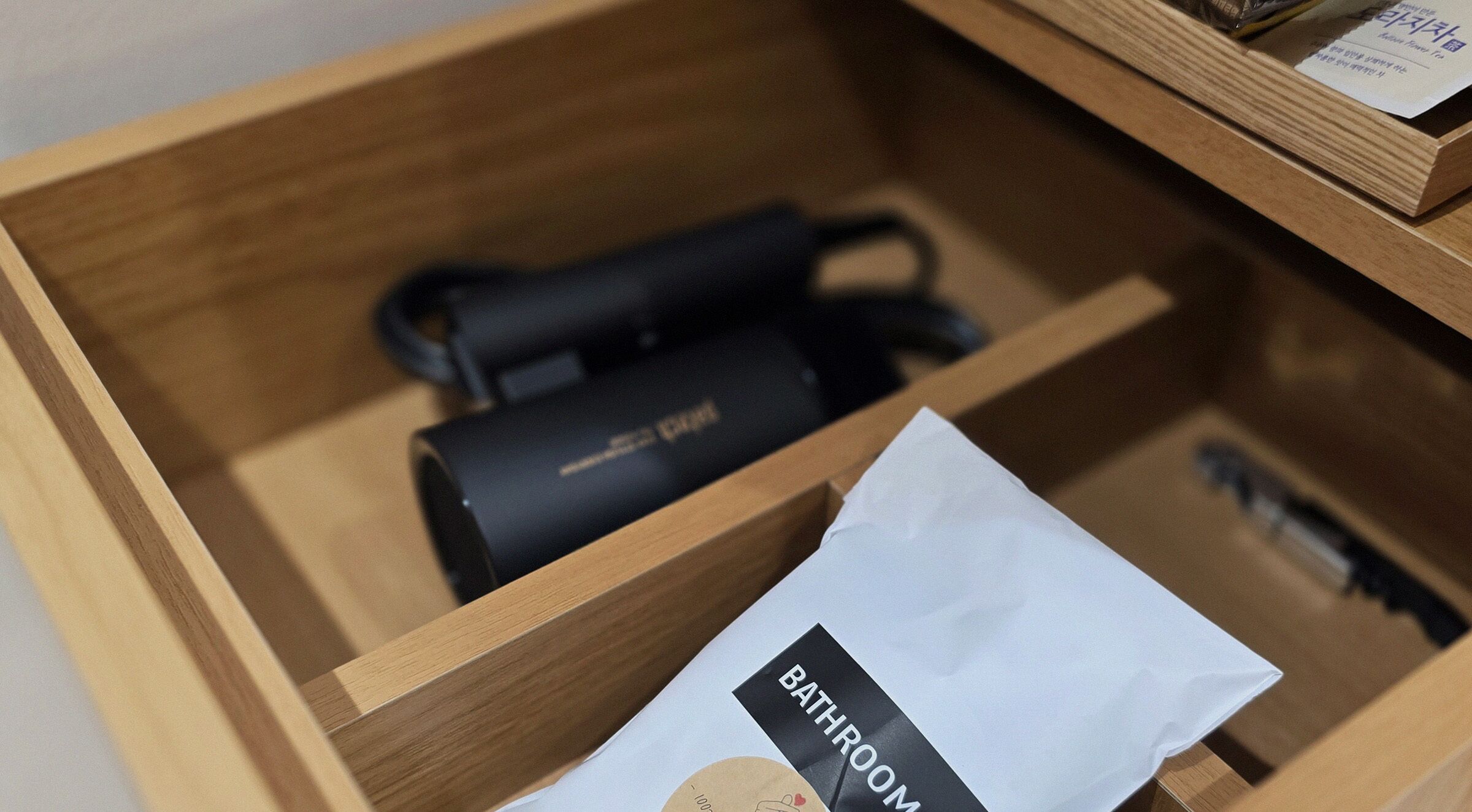 A wooden drawer with a black object and a white paper bag labeled "BATHROOM".