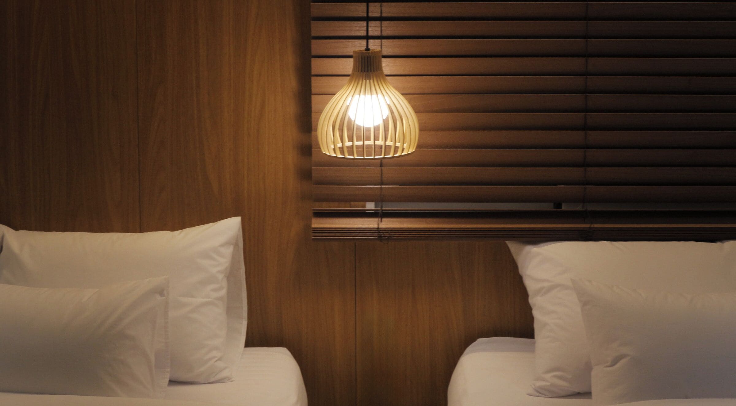A hotel room with wooden paneling, a hanging light fixture, and two beds with white bedding.