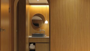 Un baño de madera con un espejo redondo, un lavamanos y un estante para toallas.
