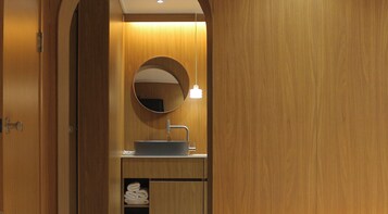 A wooden bathroom with a round mirror, a sink, and a towel shelf.