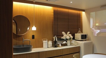 A modern bathroom with a round mirror, wooden vanity, and a microwave.