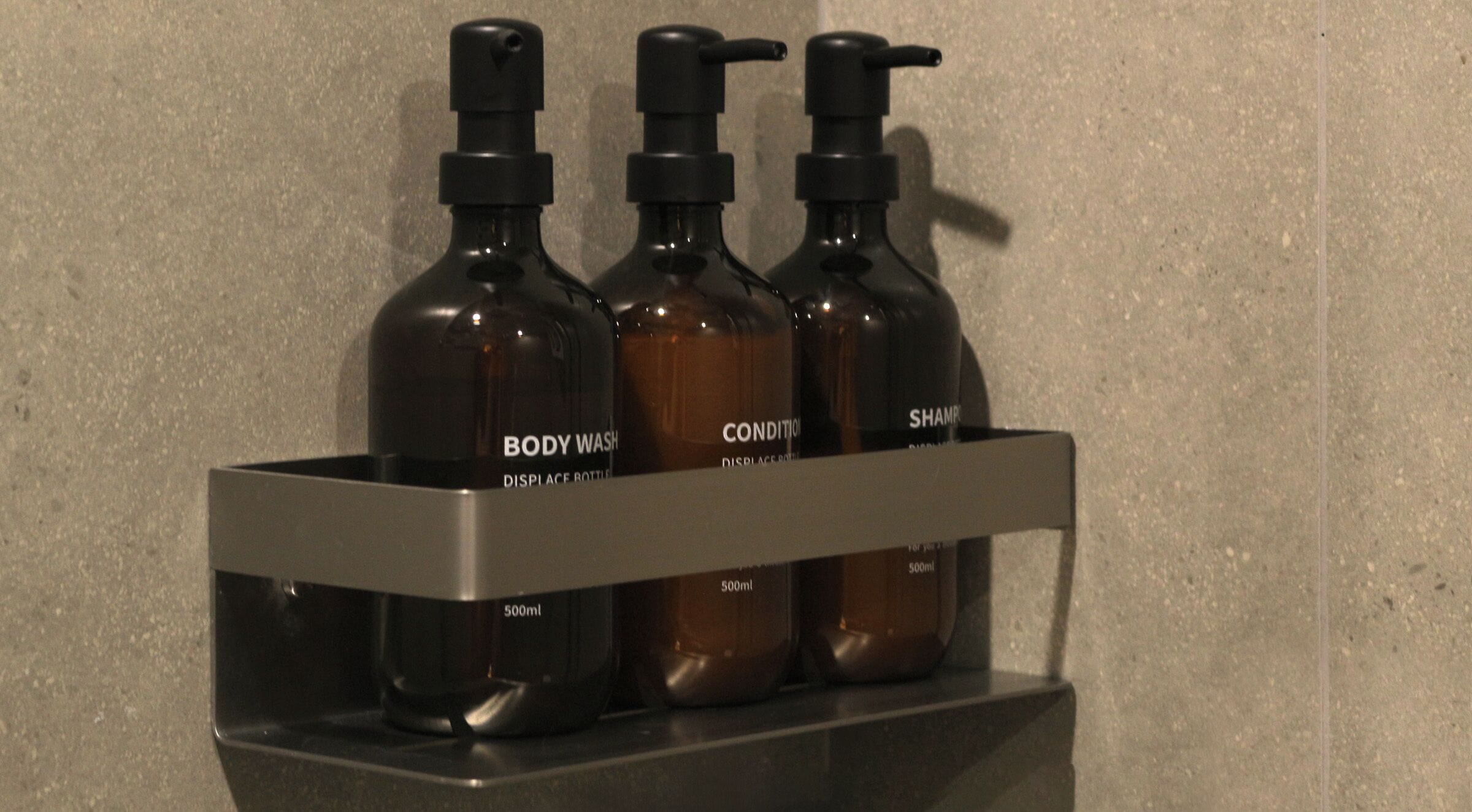 A shelf with three bottles labeled "BODY WASH," "CONDITIONER," and "SHAMPOO."