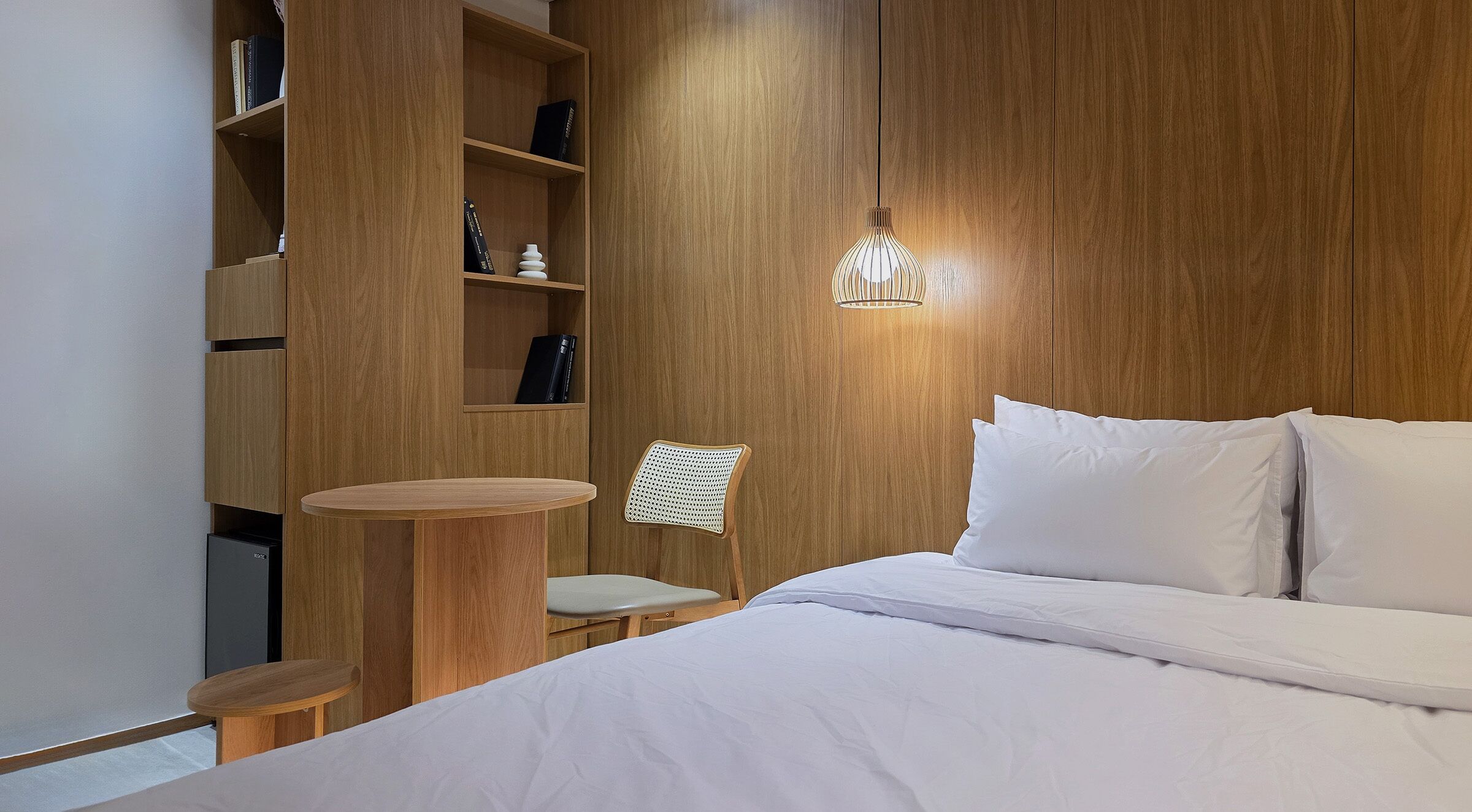 Ein Schlafzimmer mit einem Bett, einem Sessel, einem kleinen Tisch und einer Holzregalanlage mit Büchern und Dekoration.