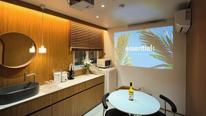 Una cocina moderna con armarios de madera, un lavamanos, un microondas y una pantalla de proyección que muestra la palabra 'essential' con hojas de palma.