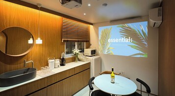 A modern kitchen with wooden cabinets, a sink, a microwave, and a projection screen displaying the word "essential" with palm leaves.