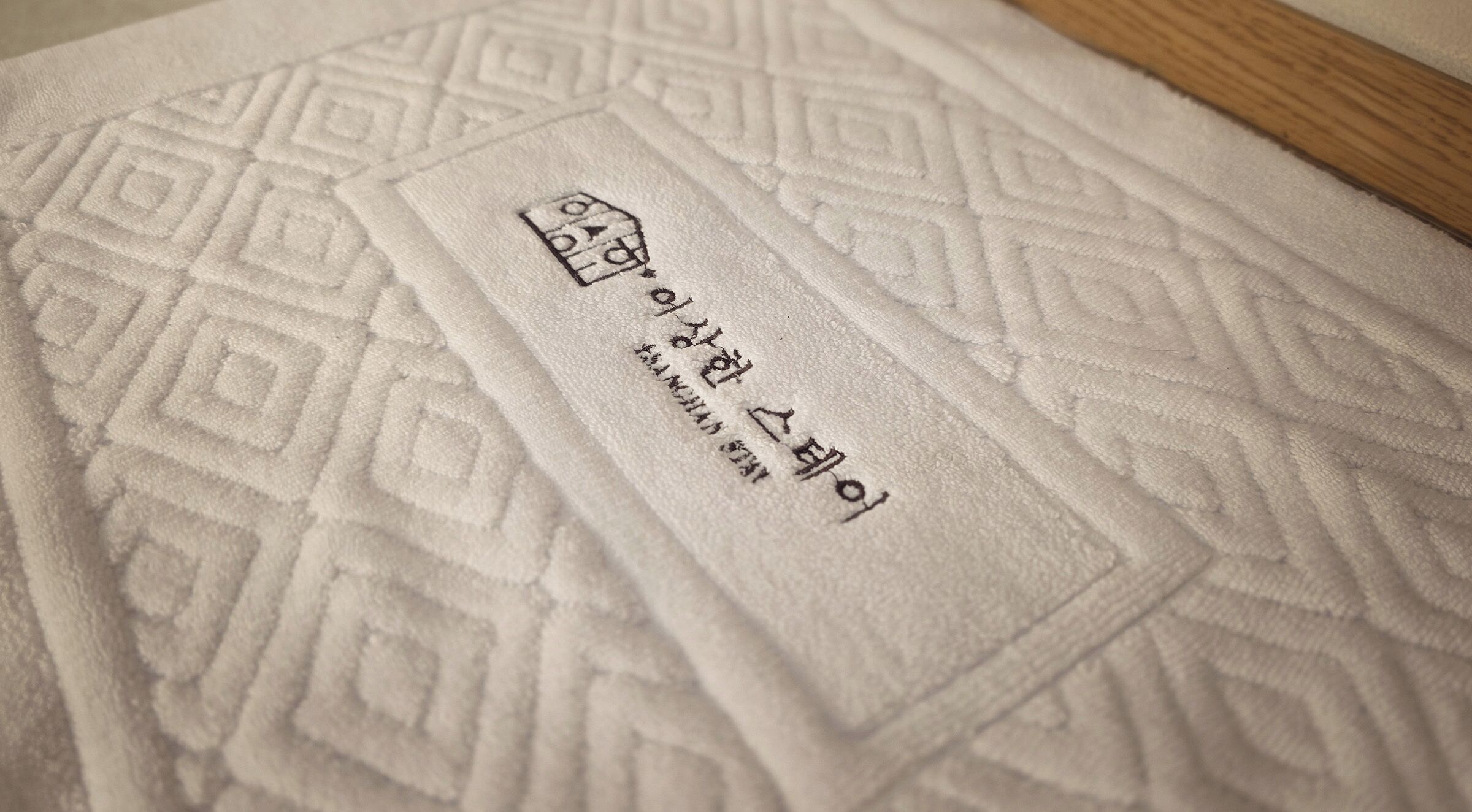 Tejido blanco con textura y un estampado geométrico, y una etiqueta con texto coreano.