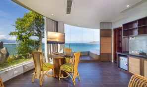 A balcony with a dining table, chairs, a TV, and a view of the sea. - MissBamboo Hotel Nha Trang (Nha Trang)
