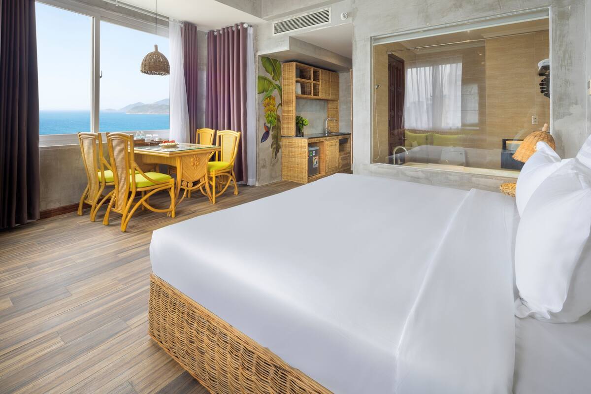 Une chambre d’hôtel dotée d’un grand lit, d’un coin repas avec des chaises, d’un coin cuisine et offrant une vue sur la mer.