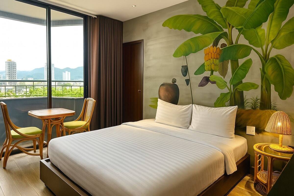 Une chambre d’hôtel avec un grand lit, une petite table avec des chaises, une table de chevet avec une lampe et une fresque représentant une plante.