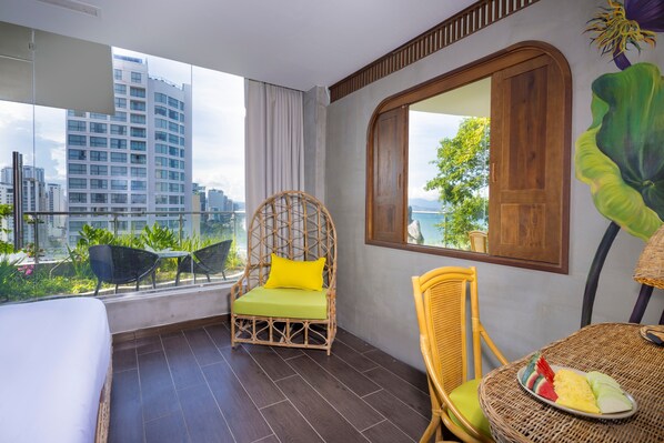 A balcony with wicker furniture, a bed, and a view of a cityscape. - MissBamboo Hotel Nha Trang (Nha Trang)