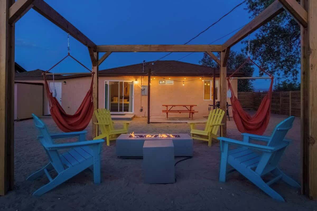 A covered outdoor patio with a fire pit, two blue Adirondack chairs, and a yellow chair.