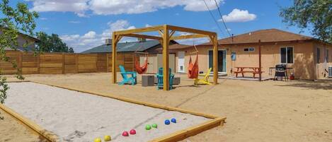 A backyard with a wooden pergola, colorful chairs, a sandbox, and a barbecue area.