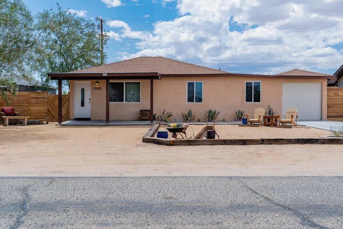 Une maison de plain-pied avec un garage, une véranda à l’avant avec une table et des chaises, et un petit jardin.