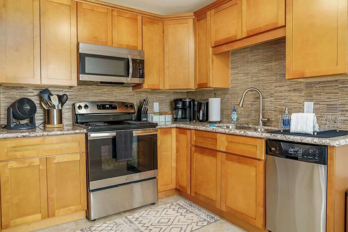Una cocina moderna con armarios de madera, electrodomésticos de acero inoxidable, microondas, horno, lavavajillas y una encimera de granito.