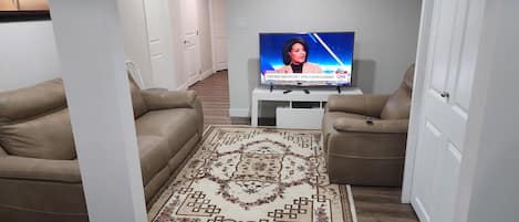 A living room with two leather sofas, a patterned rug, and a television displaying a news channel.