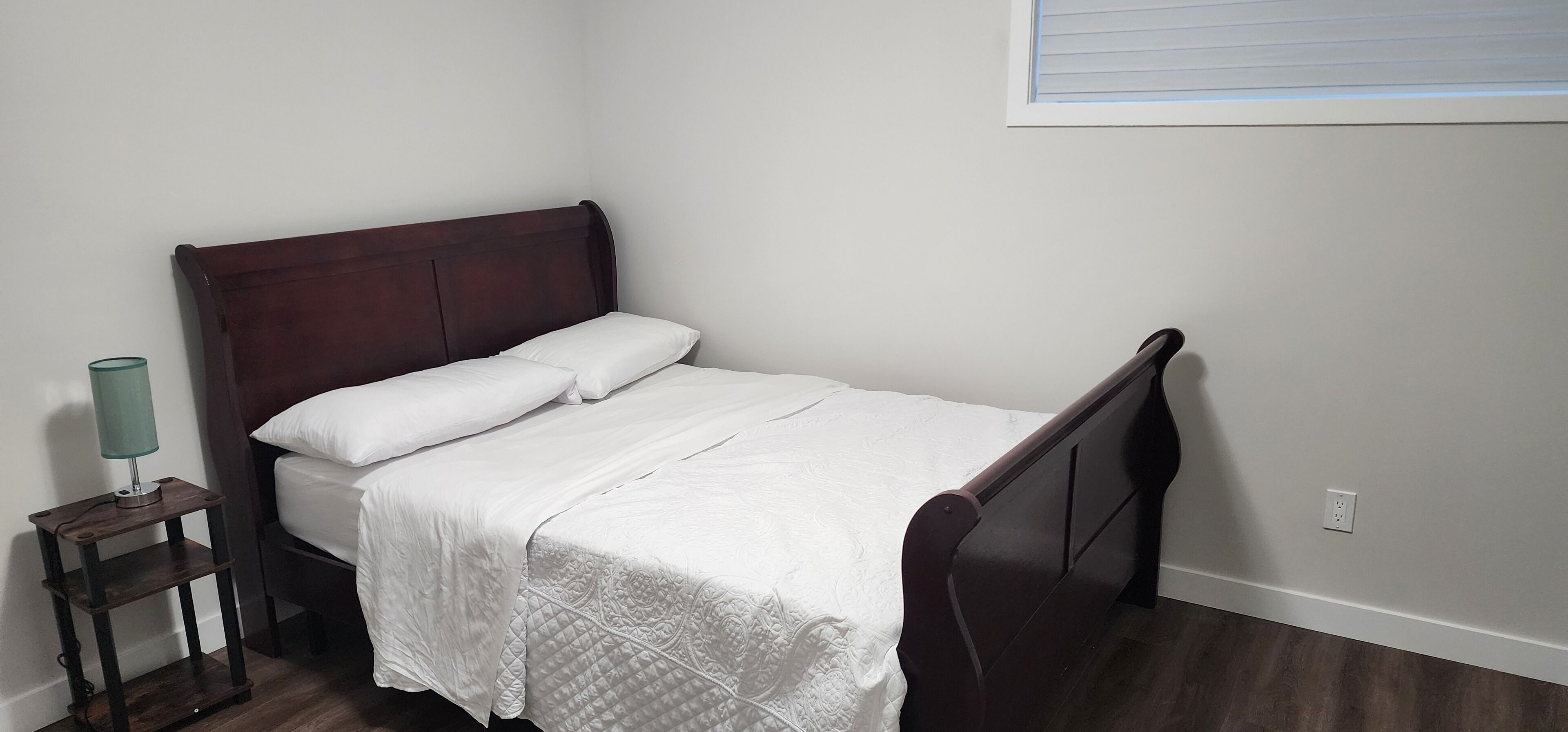 A single bed with a wooden headboard, white bedding, and a small bedside table with a lamp.