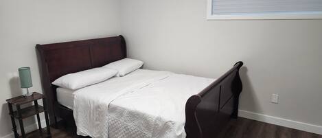 A single bed with a wooden headboard, white bedding, and a small bedside table with a lamp.