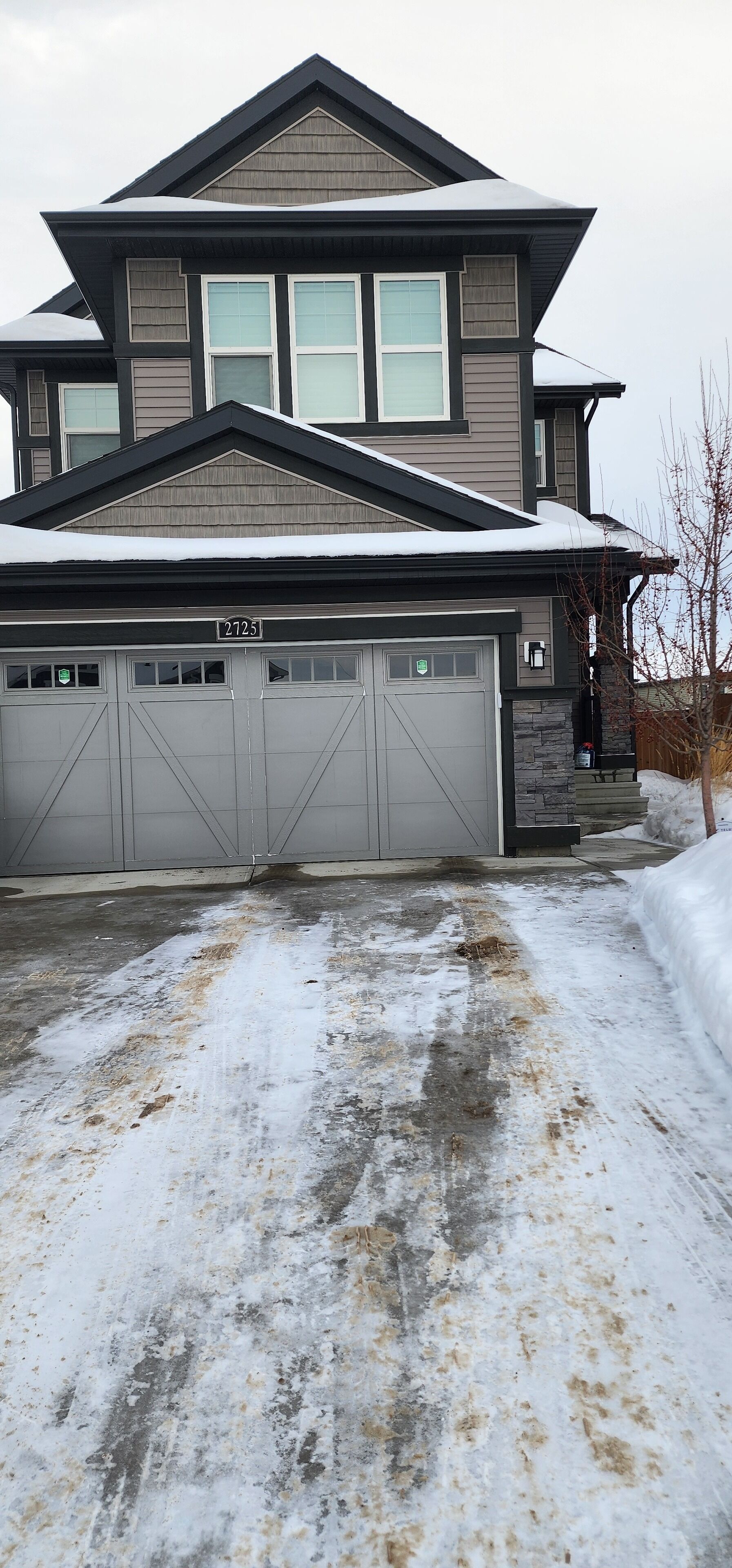 A two-story house with a garage, a number plate, and a snow-covered driveway.
