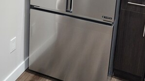 A stainless steel refrigerator in a kitchen with a wooden floor and white walls. - CNEORM HAVEN (Edmonton)