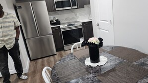 A modern kitchen with stainless steel appliances, a round table with a placemat, and a vase with flowers. - CNEORM HAVEN (Edmonton)