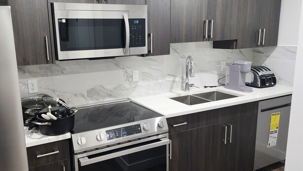 A modern kitchen with a built-in microwave, stainless steel appliances, and a marble countertop. - CNEORM HAVEN (Edmonton)