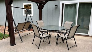 Eine Terrasse mit einem runden Tisch, vier Stühlen, einer Schaukel und einer Glasschiebetür.