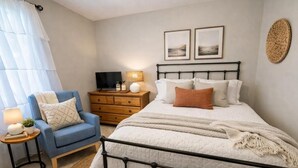 Ein Schlafzimmer mit einem Bett, einem Sessel, einem Nachttisch, einem Fernseher und Bildern an der Wand.