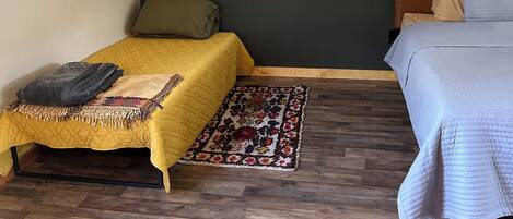 Una habitación pequeña y acogedora con dos camas, piso de madera y una pared de acento verde oscuro.