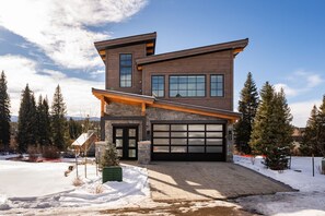Uma casa moderna de dois andares com garagem, cercada por neve e árvores.