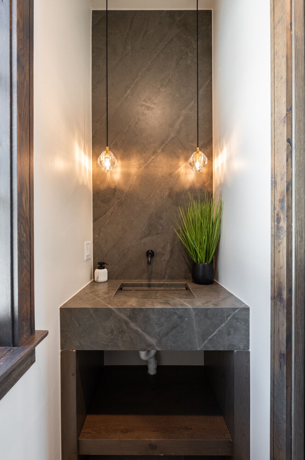 A modern bathroom with a dark marble sink, two pendant lights, and a potted plant.