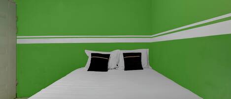 A room with green walls, a white bedspread, and black and white pillows.