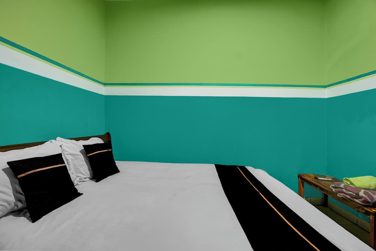 Una habitación con paredes color turquesa, una cama con ropa de cama blanco y negro, y una mesita de noche de madera con una toalla.