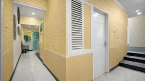 A hallway with yellow brick walls, white doors, and tiled flooring. - OYO 3738 Pemda 22 Mansion (Bogor)