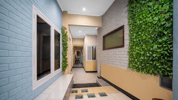 A narrow hallway with a blue wall, a brick wall with green foliage, and a tiled floor with a drain. - OYO 3738 Pemda 22 Mansion (Bogor)