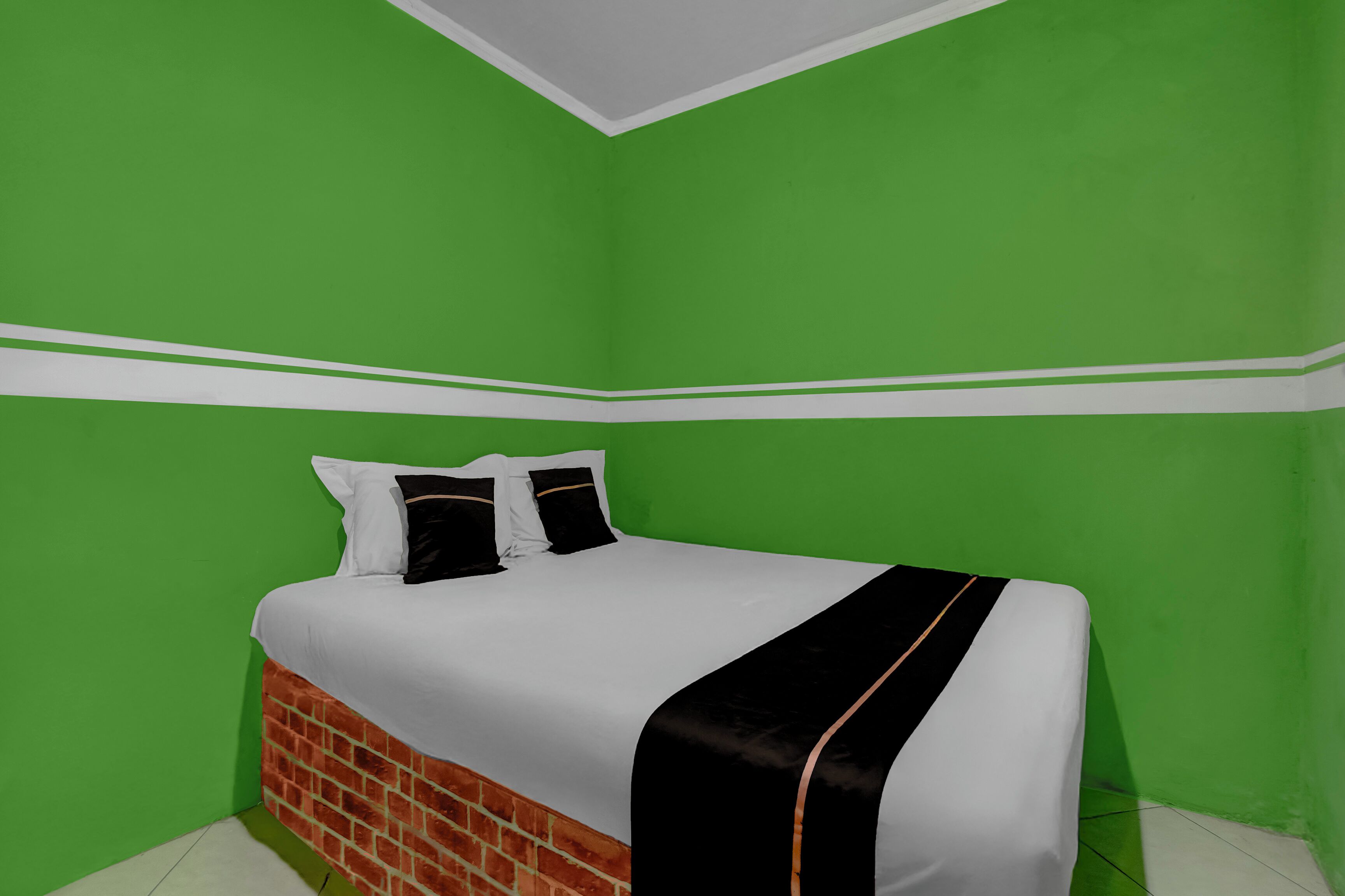 A room with a bed against a green wall, white trim, and a brick headboard.