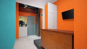 A hallway with a teal wall, an orange wall, a wooden cabinet, a white door, and a black TV mounted on the orange wall. - OYO 3738 Pemda 22 Mansion (Bogor)