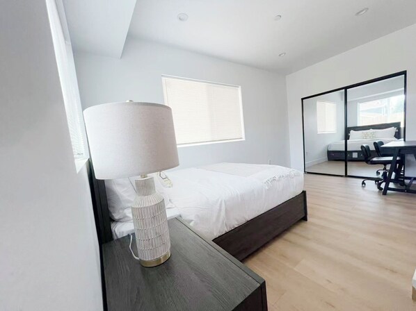 Un dormitorio moderno con cama, mesita de noche, lámpara y un espejo grande.