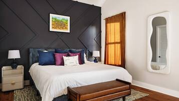 A bedroom with a bed, bedside tables, a bench, a wall-mounted mirror, and a window with curtains.